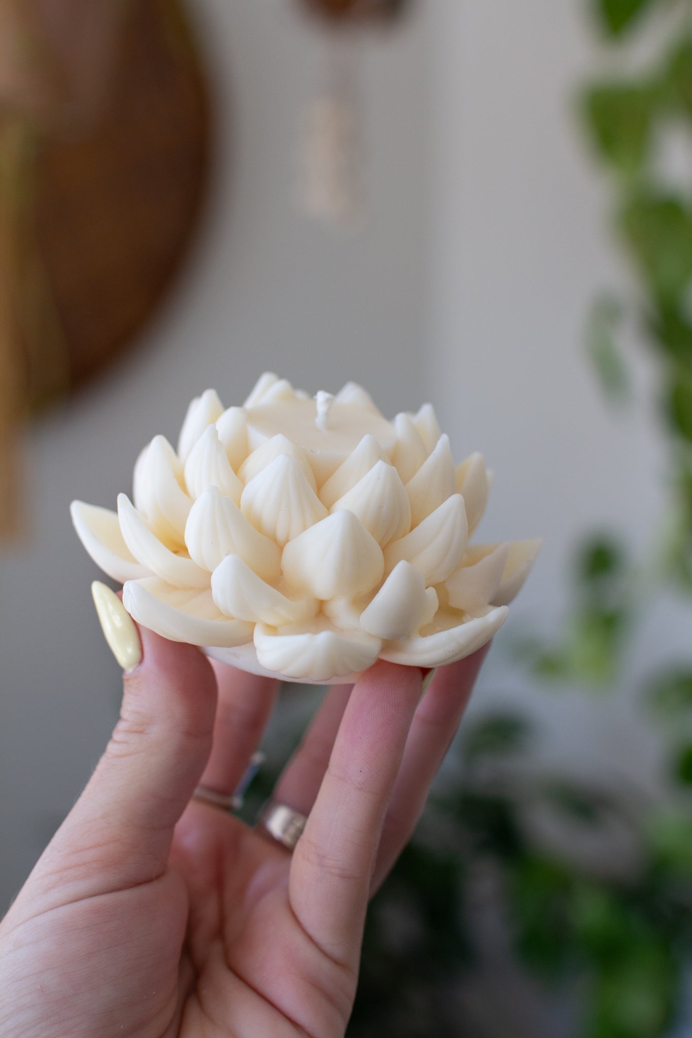 Hand holding a soy wax lotus flower candle against a blurred indoor background