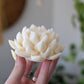 Hand holding a soy wax lotus flower candle against a blurred indoor background