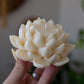 Hand holding a handmade soy wax lotus flower sculpture candle against a blurred background