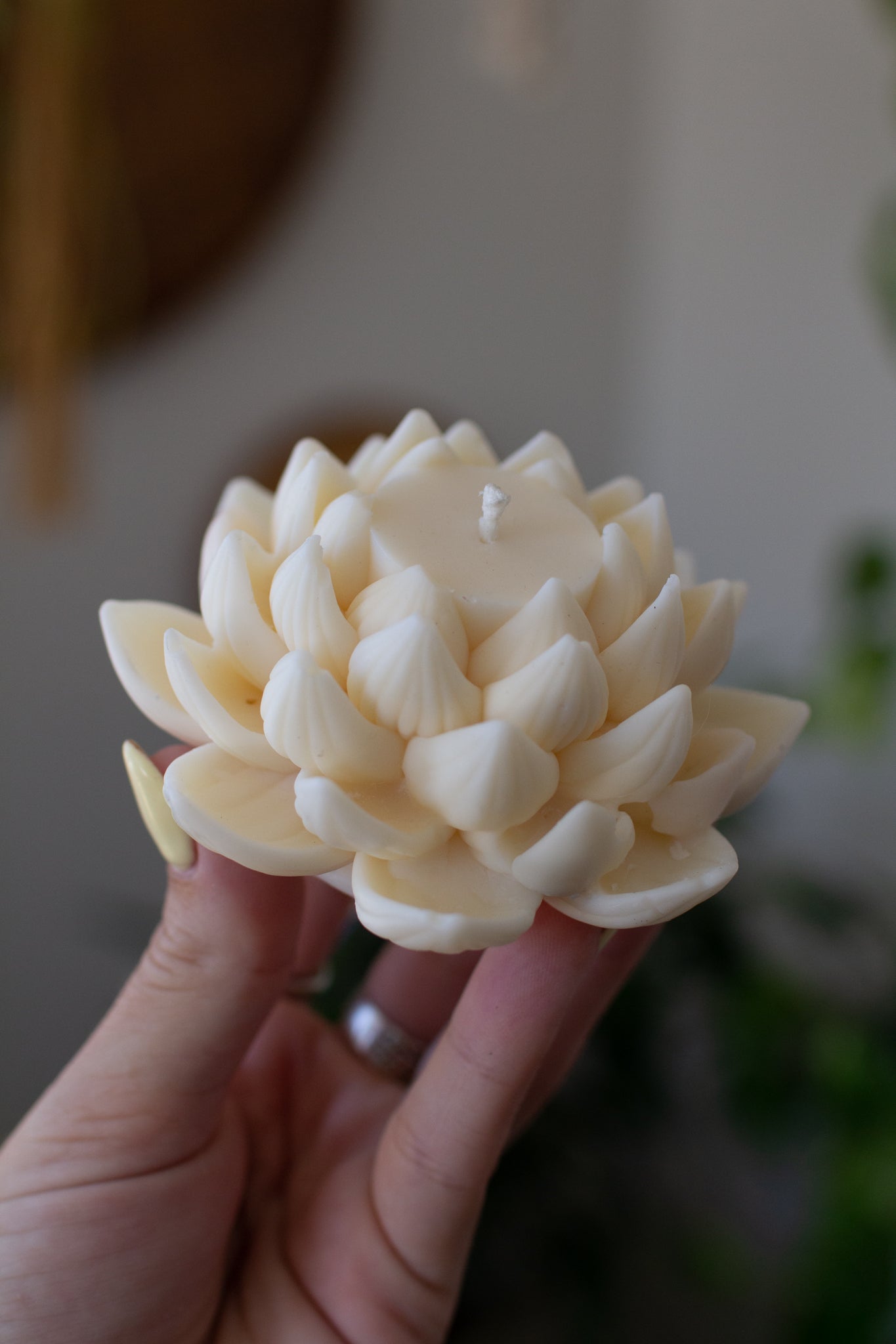 Hand holding a handmade soy wax lotus flower sculpture candle against a blurred background